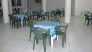 Un espace repas comprenant plusieurs tables et chaises, un sol carrelé de carreaux blancs et des murs blancs.