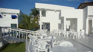 Une terrasse extérieure avec des chaises et des tables en plastique blanc, un palmier et un bâtiment blanc agrémenté de touches de bleu.