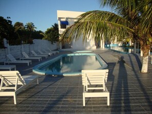 Una piscina con sillas de descanso, palmeras y un edificio moderno al fondo.