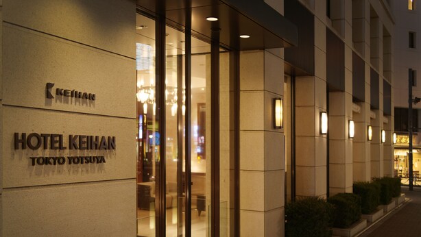 Das Hotel Keihan Tokyo Yotsuya mit moderner Fassade, großem Glastürbereich und beleuchteter Beschilderung.