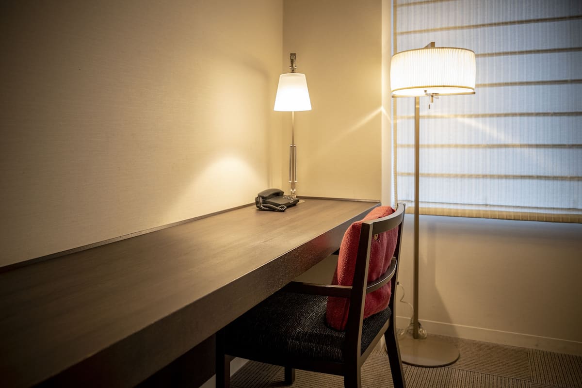 Una habitación de hotel con un escritorio de madera, una silla con una toalla roja, una lámpara y un teléfono.