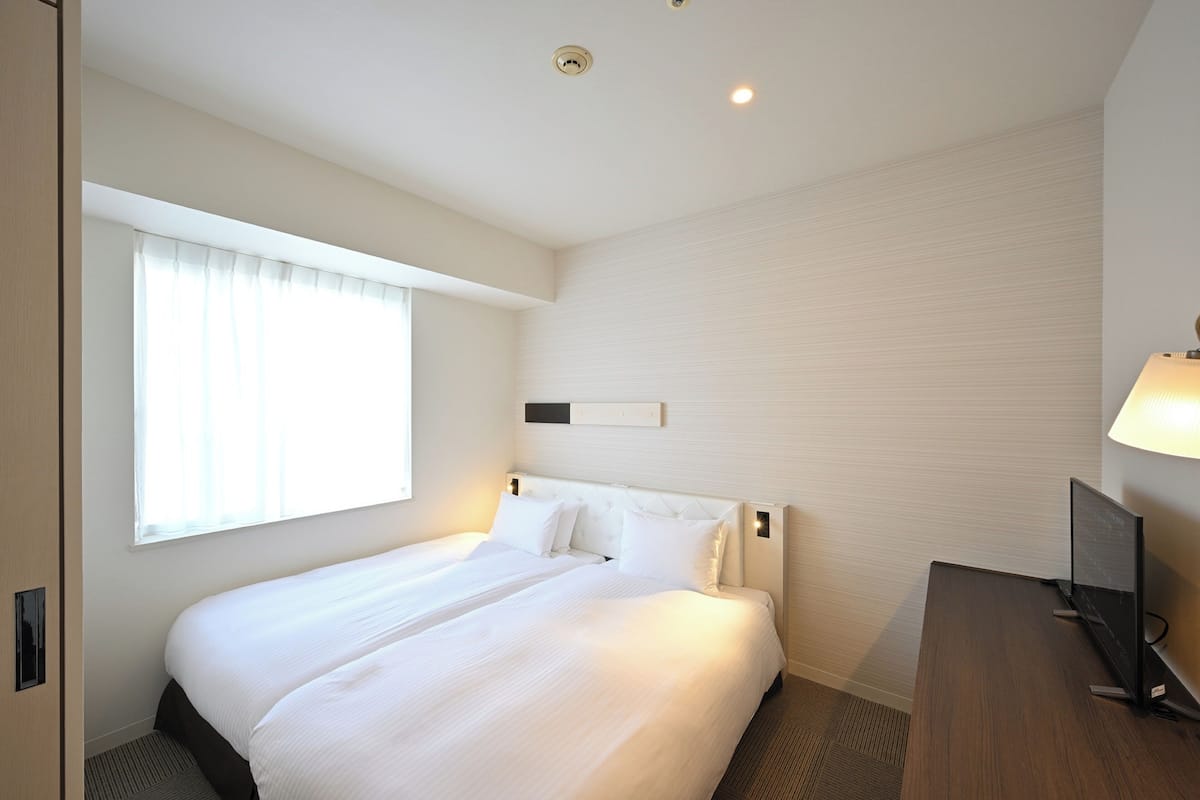 Habitación de hotel con una cama grande, un escritorio, un televisor y un ventanal con cortinas.