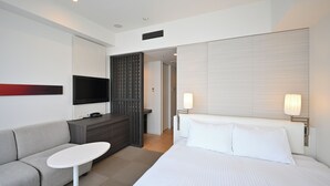 Une chambre d’hôtel moderne équipée d’un lit, d’un canapé, d’une petite table, d’une télévision et d’une lampe.