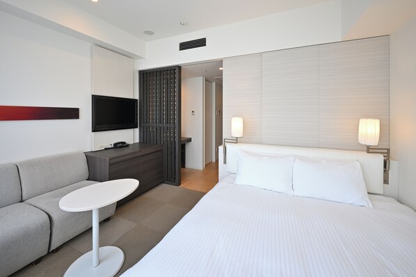 Une chambre d’hôtel moderne équipée d’un lit, d’un canapé, d’une petite table, d’une télévision et d’une lampe.