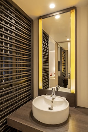 Une salle de bain moderne avec un lavabo rond, un grand miroir et une cloison en lattes de bois.
