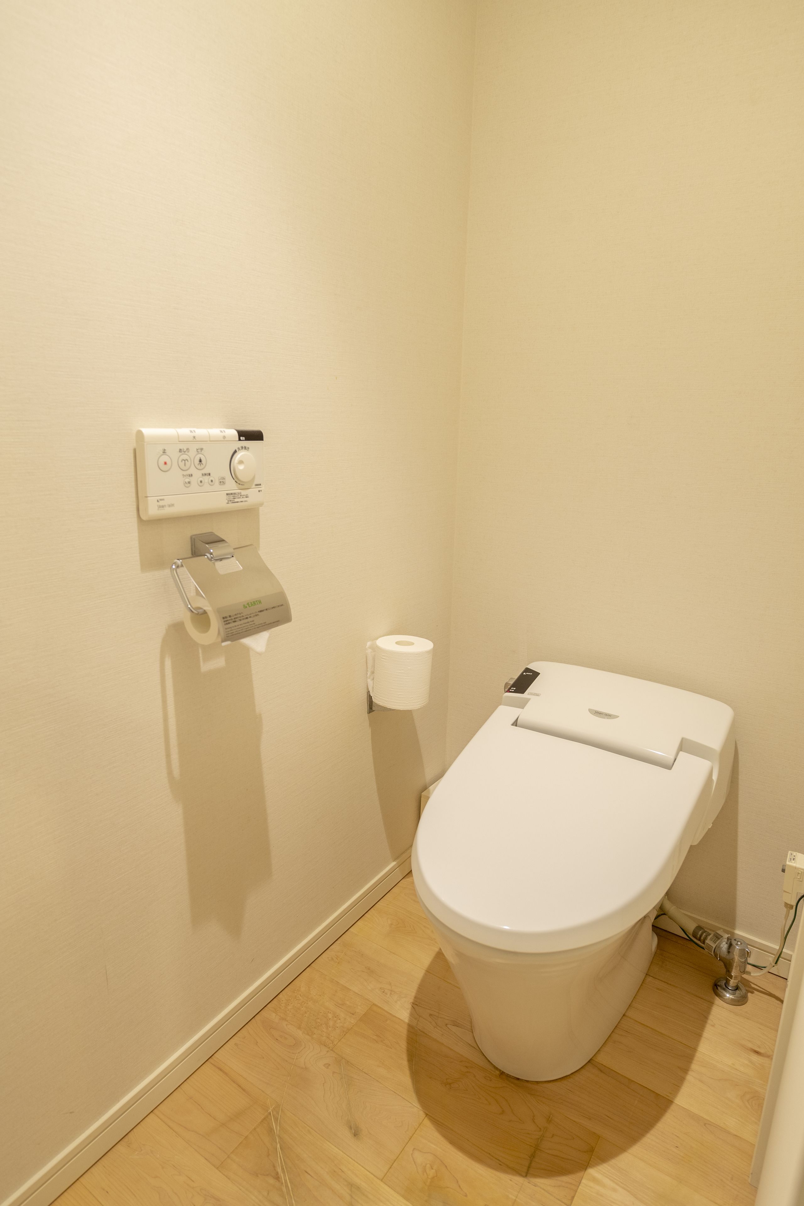 A small, clean bathroom with a toilet, a paper towel dispenser, and a toilet paper roll on the wall.