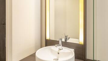 Un baño moderno con un lavamanos blanco, un espejo con luz amarilla y un sistema de ventilación en el techo.