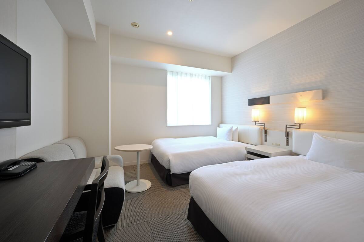 Una habitación de hotel con dos camas, un escritorio, una silla, una mesita y un televisor.