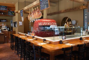 Un restaurant doté d’un long bar en bois, de chaises noires et d’un four à pizza aux couleurs rouge et blanche.