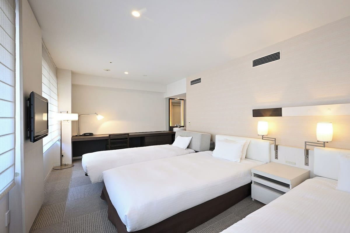 Una habitación de hotel con dos camas, un escritorio, un televisor y un espejo grande.