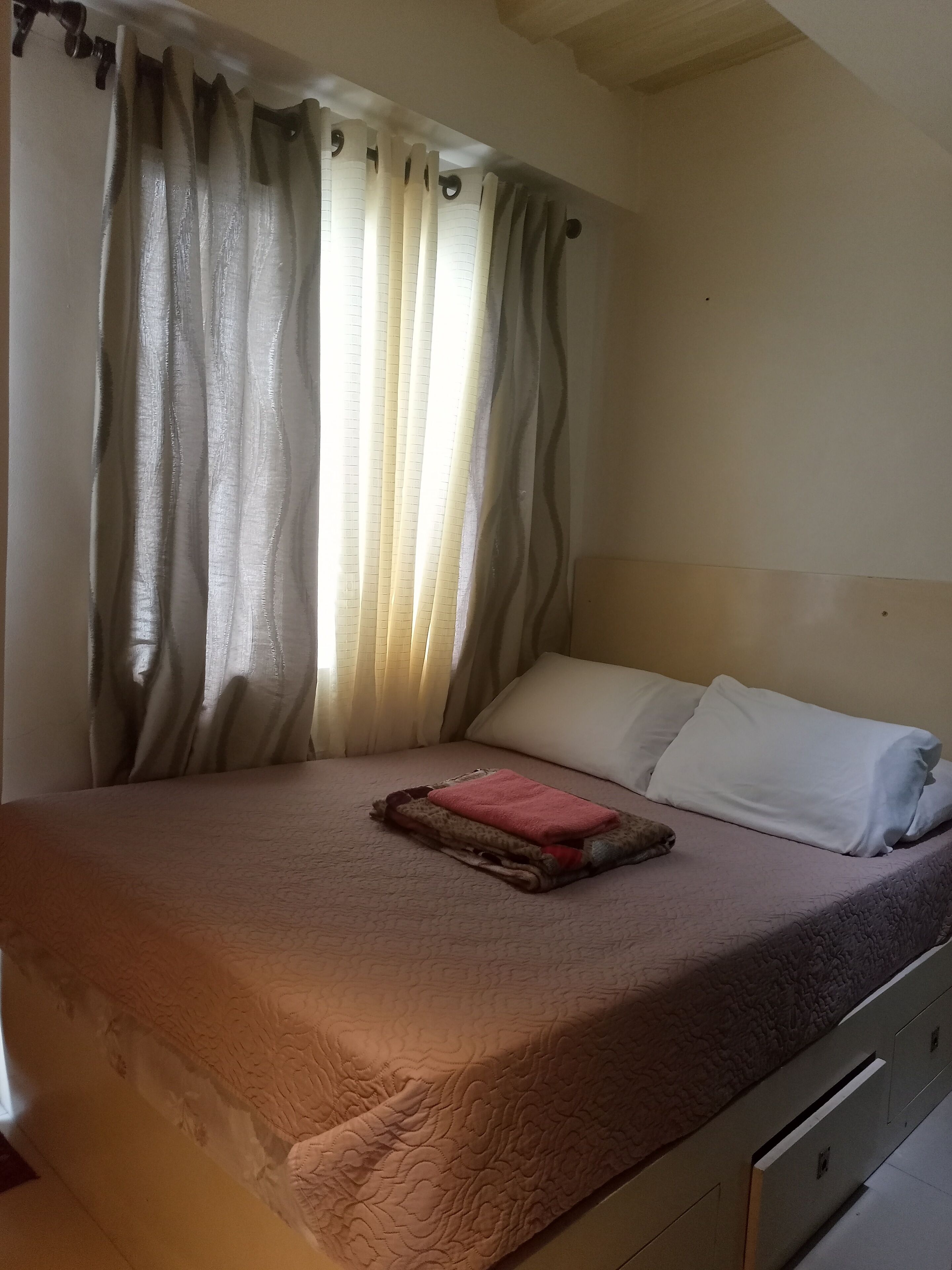 Un lit bien fait, avec une serviette rose et une couverture marron, des oreillers blancs et une tête de lit.