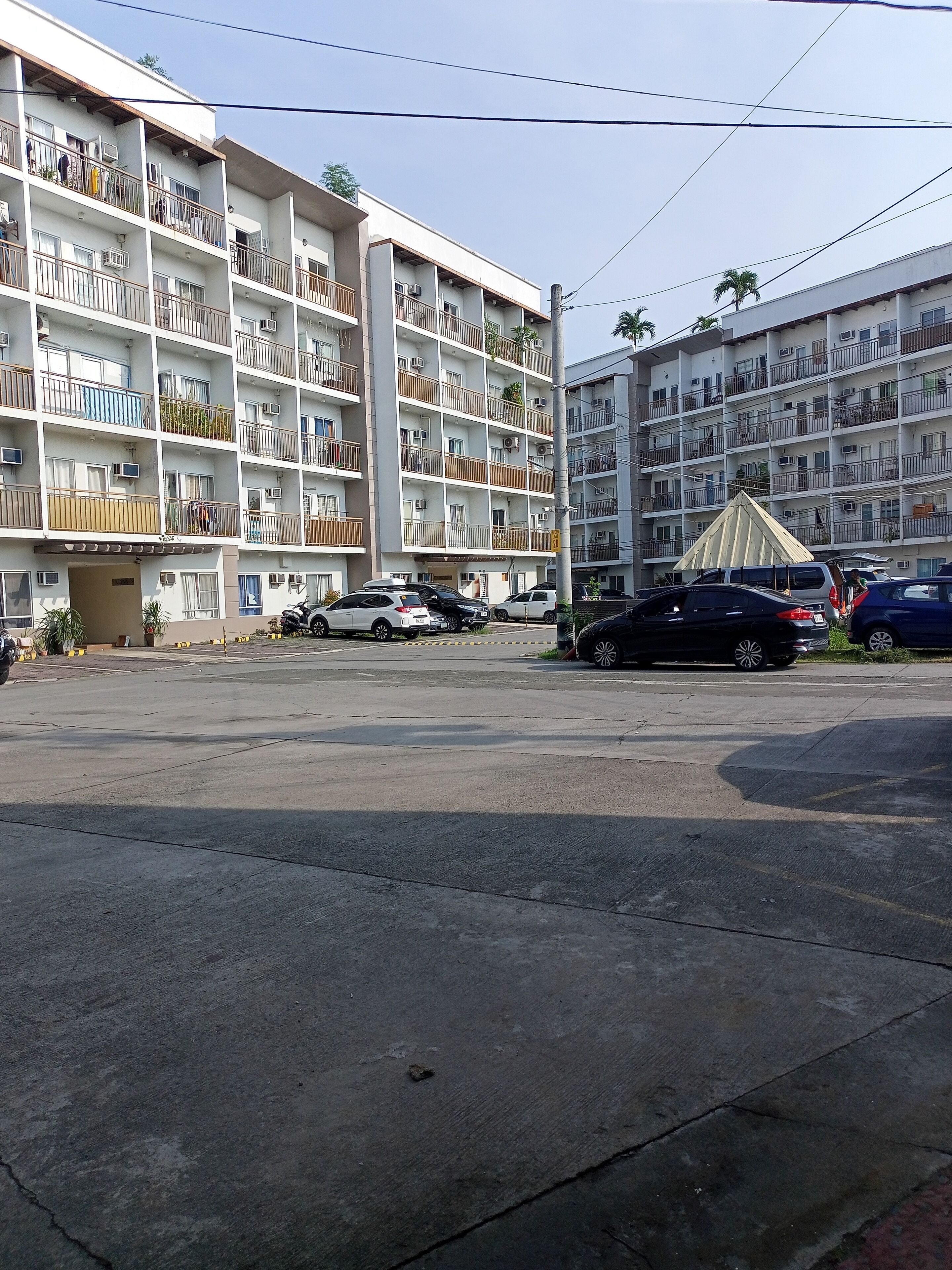 A multi-story residential building with balconies, air conditioning units, and a parking area with several cars.