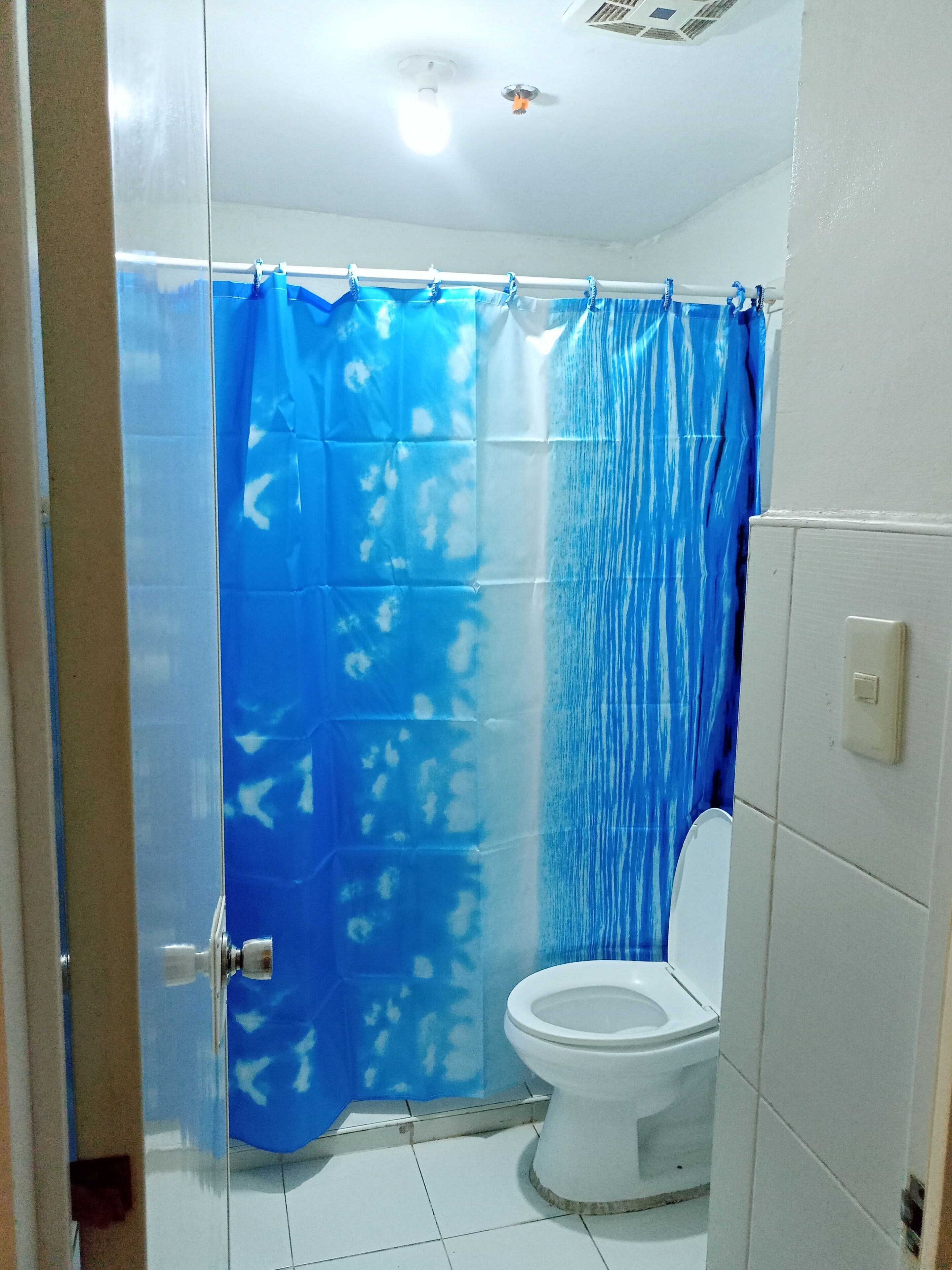 A bathroom with a white toilet, a blue shower curtain, and white tiled walls.