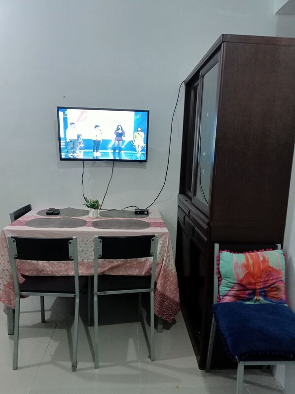 A dining area with a table, chairs, a television mounted on the wall, and a cabinet. - Angel Travellers Transit House (Parañaque)