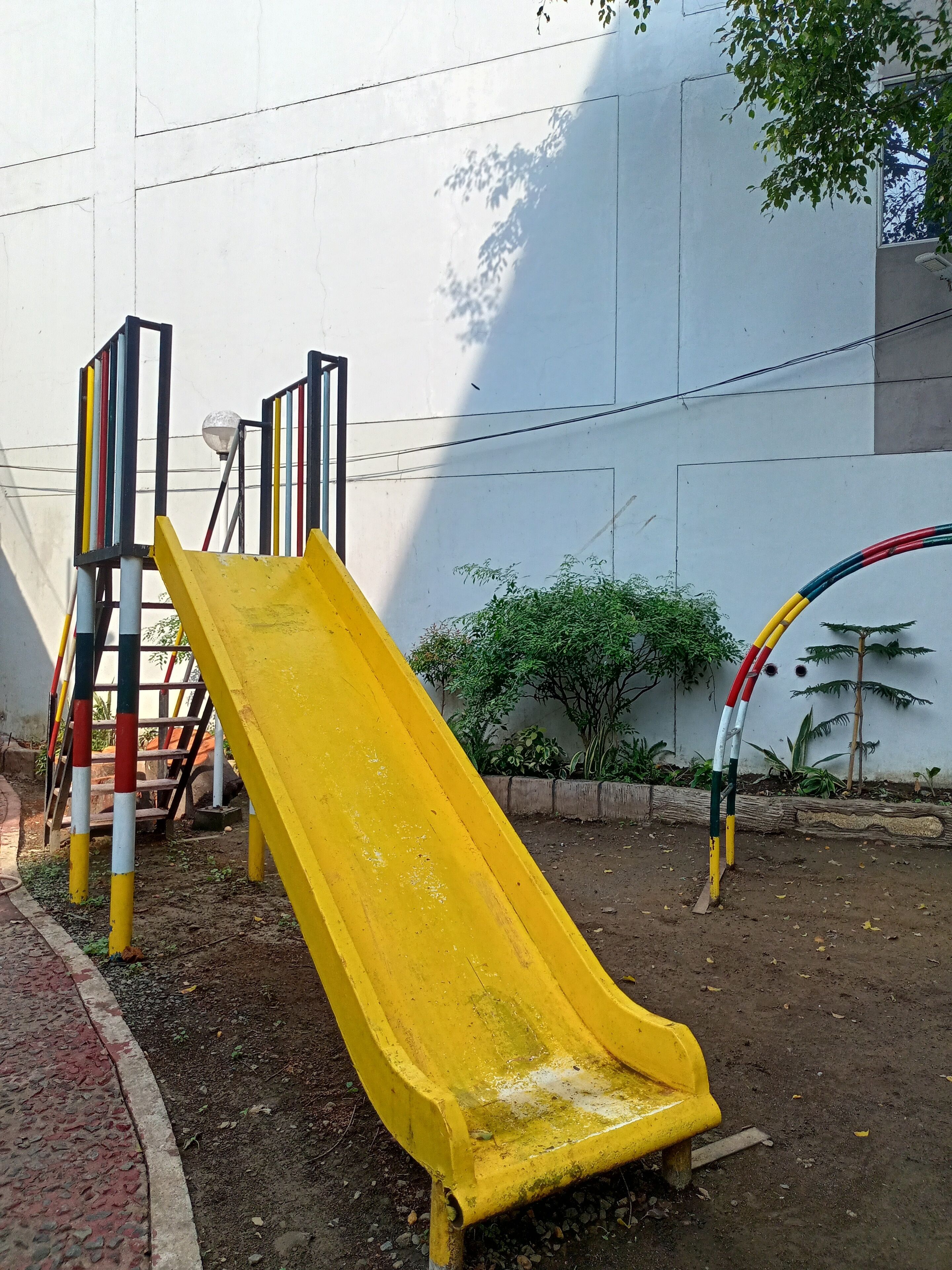 A playground with a yellow slide, a climbing structure, and a hoop.