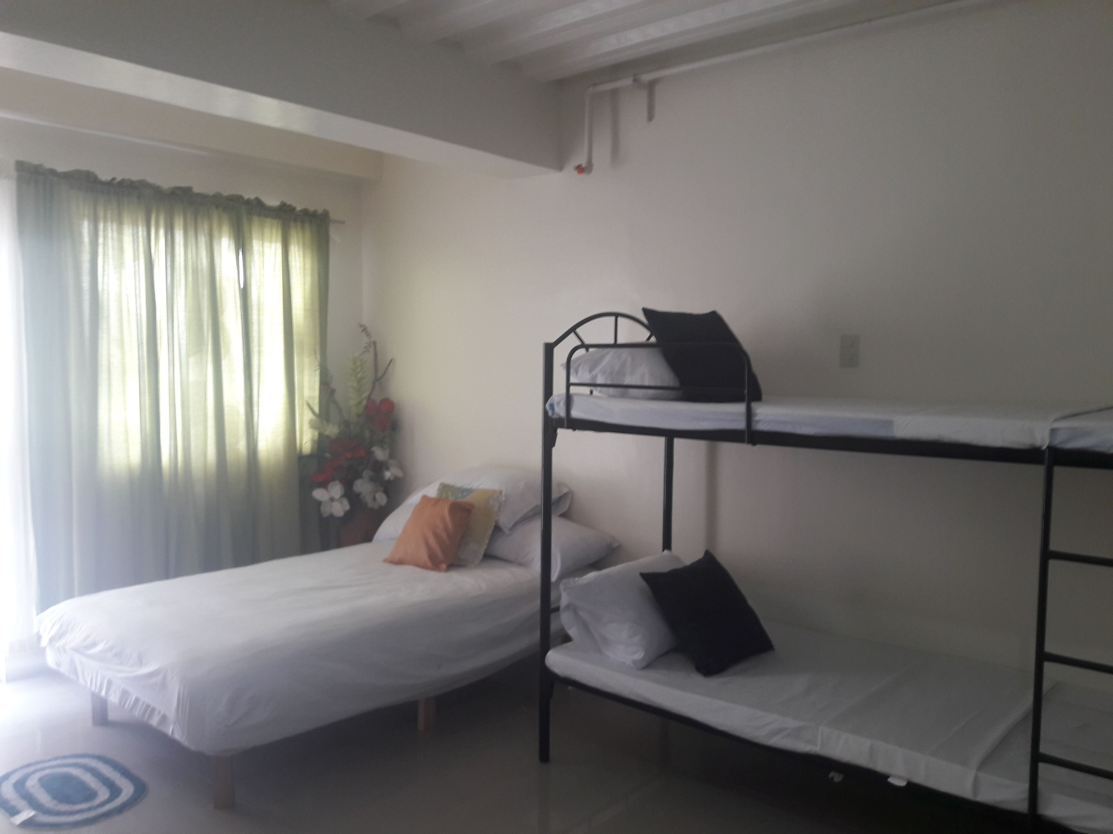 Une chambre de dortoir avec des lits superposés, une petite table de chevet et une fenêtre avec des rideaux.