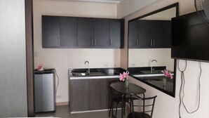 A compact kitchen with dark cabinets, a refrigerator, a sink, and a dining area with two chairs. - Angel Travellers Transit House (Parañaque)