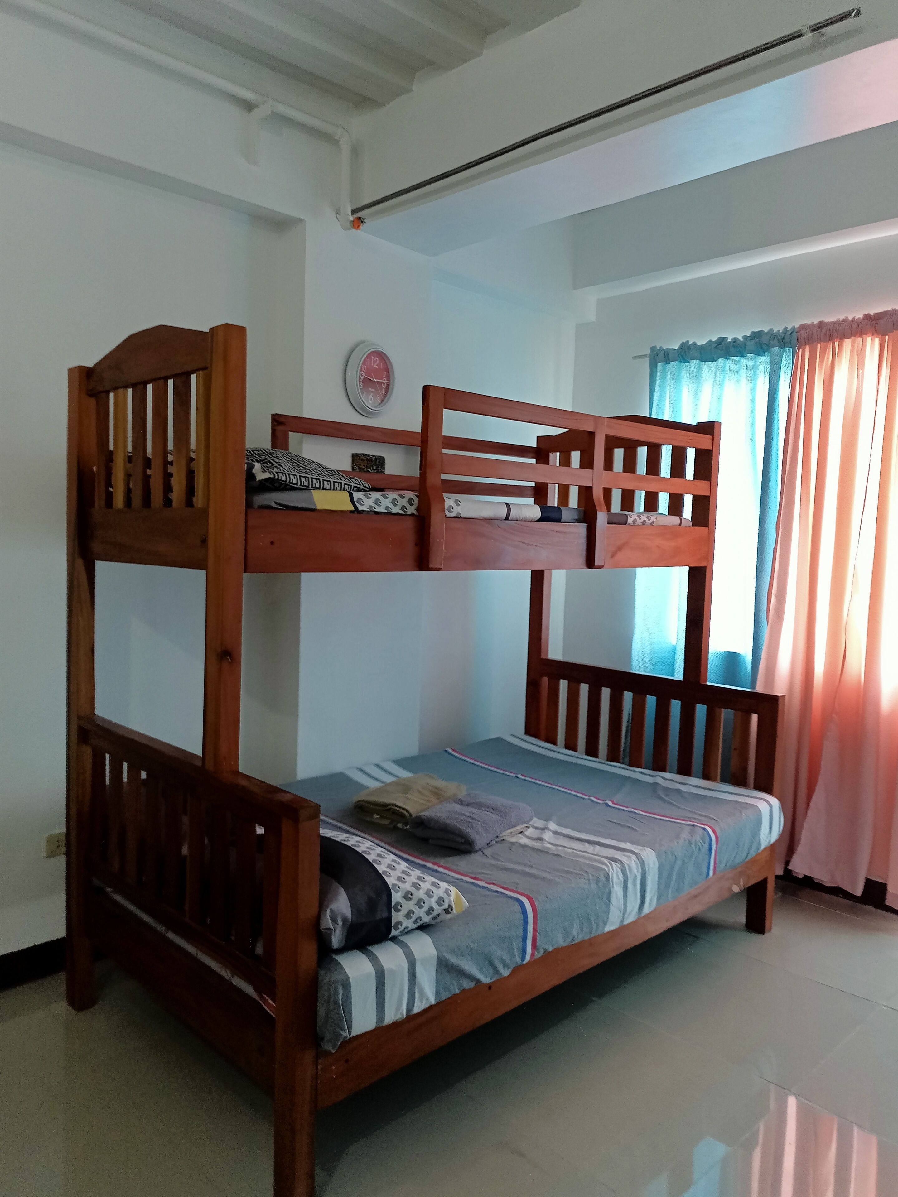 A bunk bed with a wooden frame, a clock on the wall, and a window with curtains.