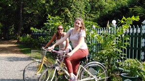 Two people riding bicycles on a gravel path surrounded by greenery and a white picket fence. - Jungle View Guest (Polonnaruwa)