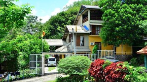 A multi-story building with a sloped roof, surrounded by lush greenery and a white fence. - Deer Point Hotel Kandy (Kandy)