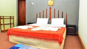 A neatly arranged bedroom with a bed, bedside tables, a wooden headboard, a red and beige bedspread, and a blue and white rug. - Deer Point Hotel Kandy (Kandy)