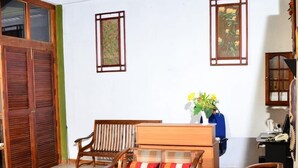A spacious room with wooden furniture, including a sofa and chairs, a dining table, and a speaker. There are two framed artworks on the walls and a wooden cabinet. - Deer Point Hotel Kandy (Kandy)