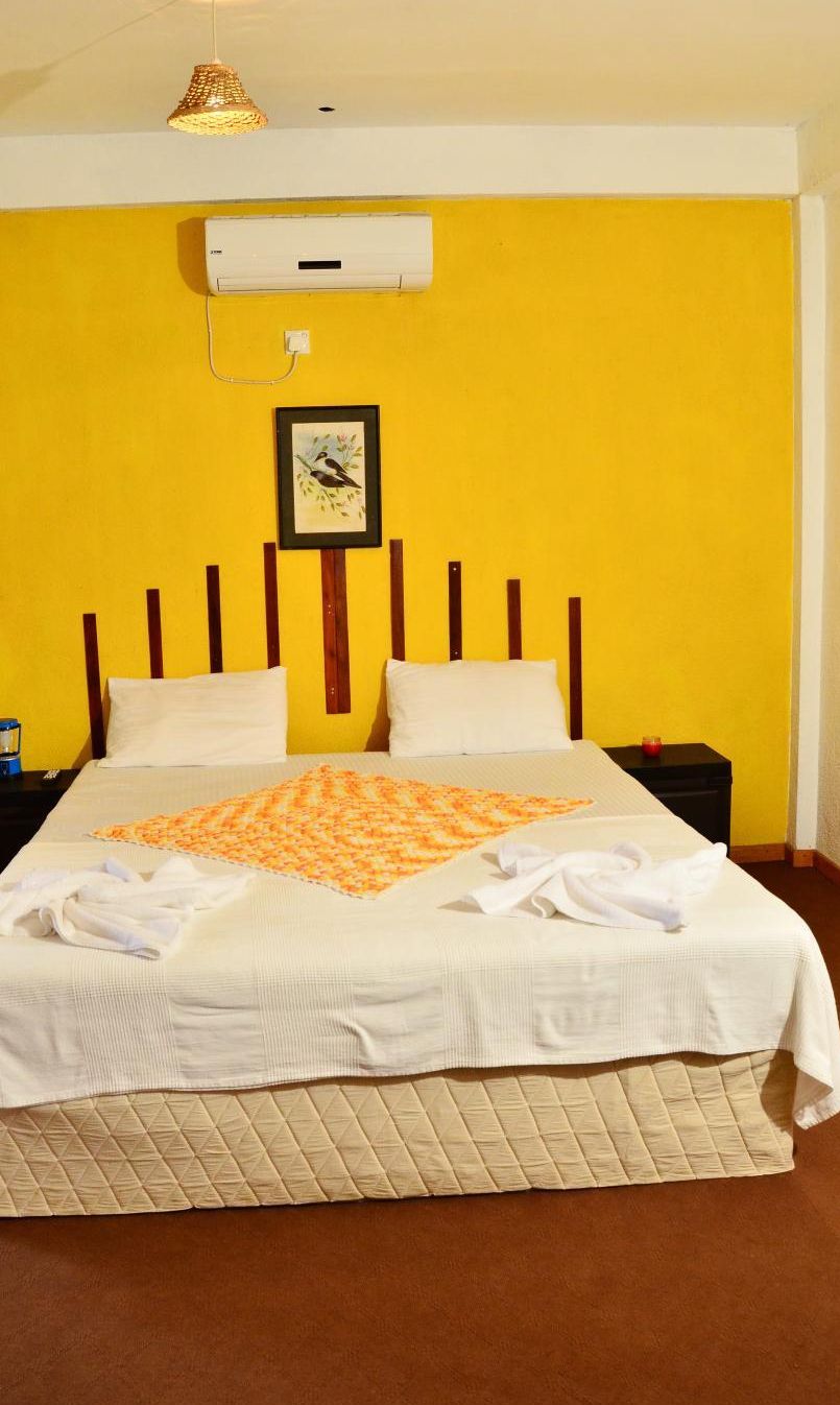 Una cama con colcha, un reloj y un aire acondicionado de pared en una habitación con paredes amarillas.