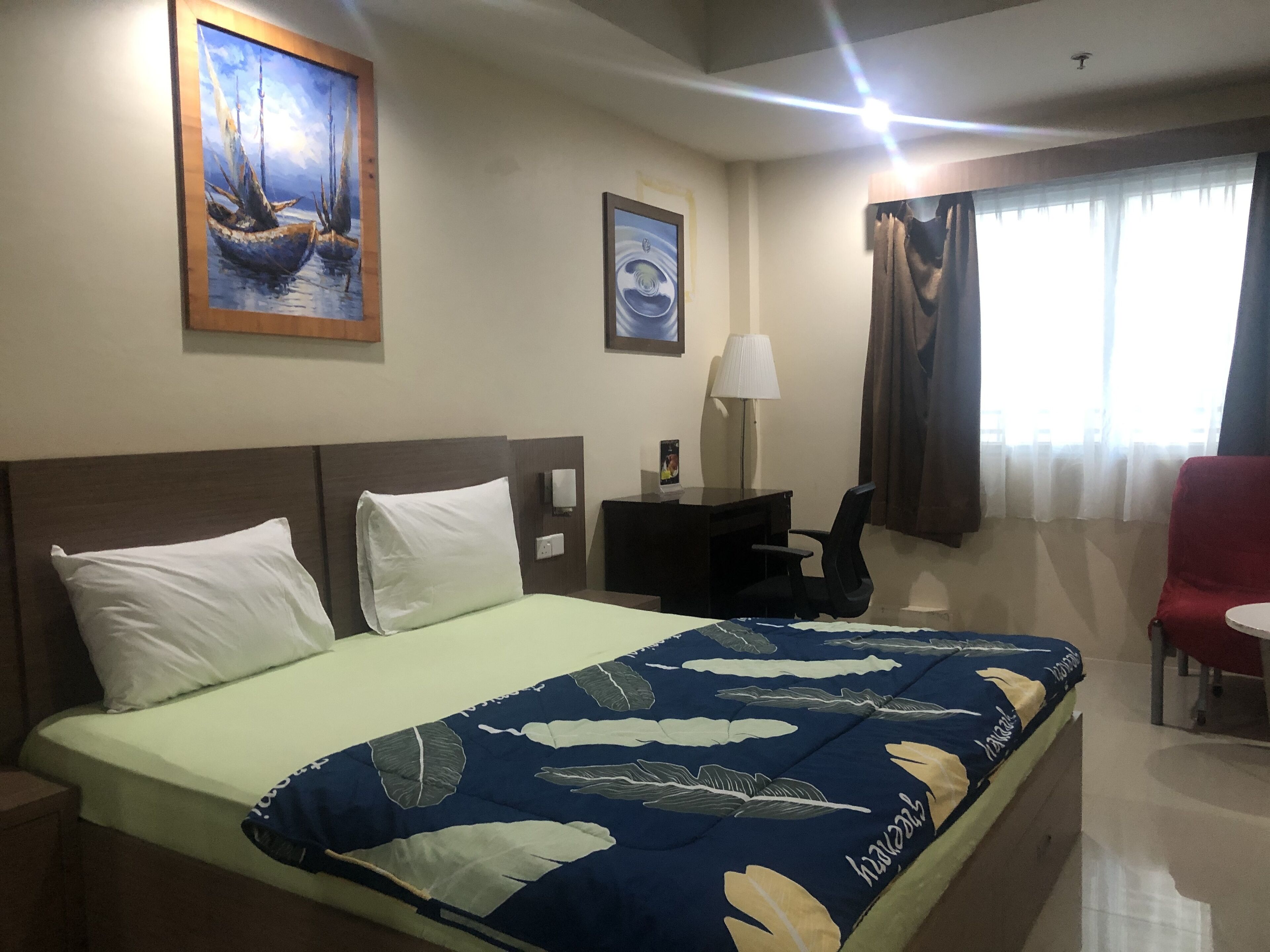 Una habitación de hotel con una cama, un escritorio, una silla y dos cuadros en la pared.