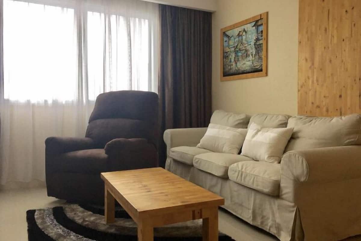 Ett vardagsrum med en mörk fåtölj, en beige soffa och ett soffbord i trä.