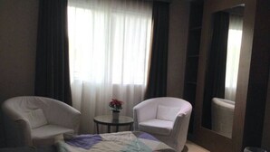 A hotel room with a bed, two white armchairs, a small round table with a plant, and a large mirror. - Studio Apartment Nagoya Mansion Batam (Batam)