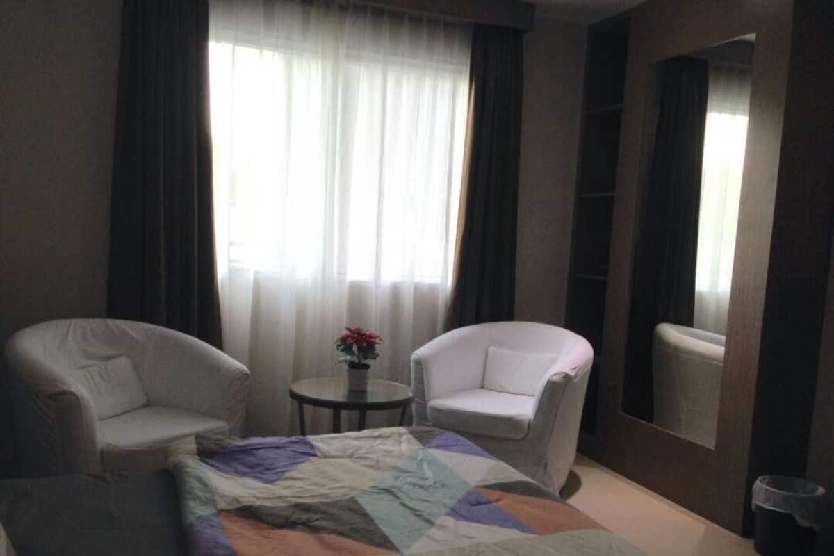 Ett hotellrum med en säng, två vita fåtöljer, ett litet runt bord med en växt och en stor spegel.