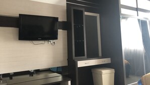 A modern room with a flat-screen TV mounted on the wall, a built-in desk with a chair, a mirror, and a trash bin. - Studio Apartment Nagoya Mansion Batam (Batam)