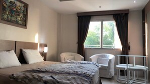 A hotel room with a large bed, a chair, a small table, and a window with curtains. - Studio Apartment Nagoya Mansion Batam (Batam)
