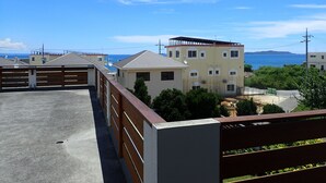 A residential area with a view of the sea, featuring modern buildings with balconies and a wooden fence. - Smilax Kurichi (Uruma)