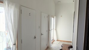 A hallway with white doors, one marked "TOILET," leading to a room with a wooden table and a window with curtains. - Smilax Kurichi (Uruma)