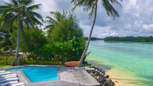 Une mer d’un bleu turquoise éclatant, une terrasse en bois avec des chaises longues et des palmiers.