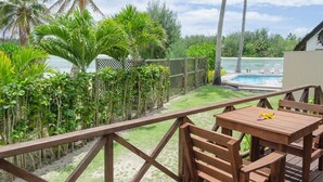 Une terrasse en bois avec une piscine et des chaises longues, entourée d’une végétation tropicale et de palmiers.