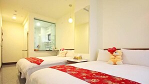 Quarto de hotel com duas camas, um espelho grande e um urso de pelúcia com travesseiro em formato de coração.