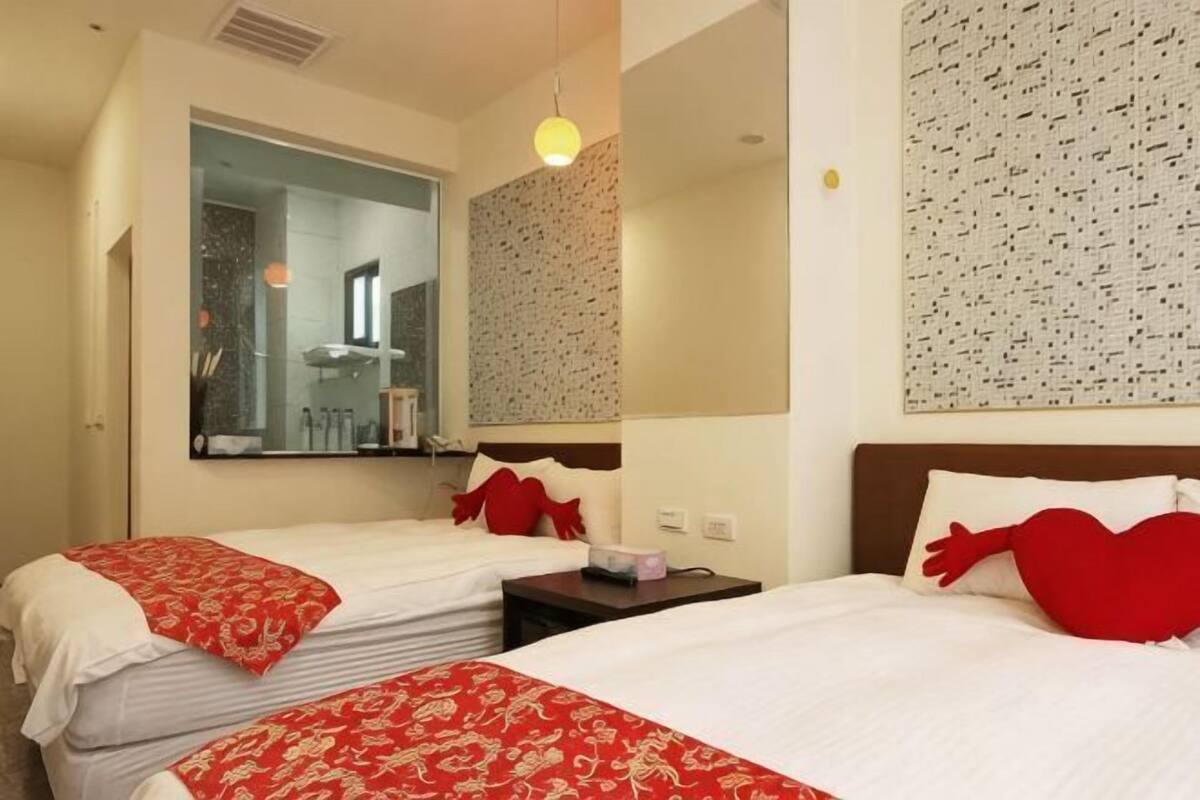 Ein Hotelzimmer mit zwei Betten, einem großen Spiegel, einer strukturierten Wand und einem kleinen Tisch mit Lampe.