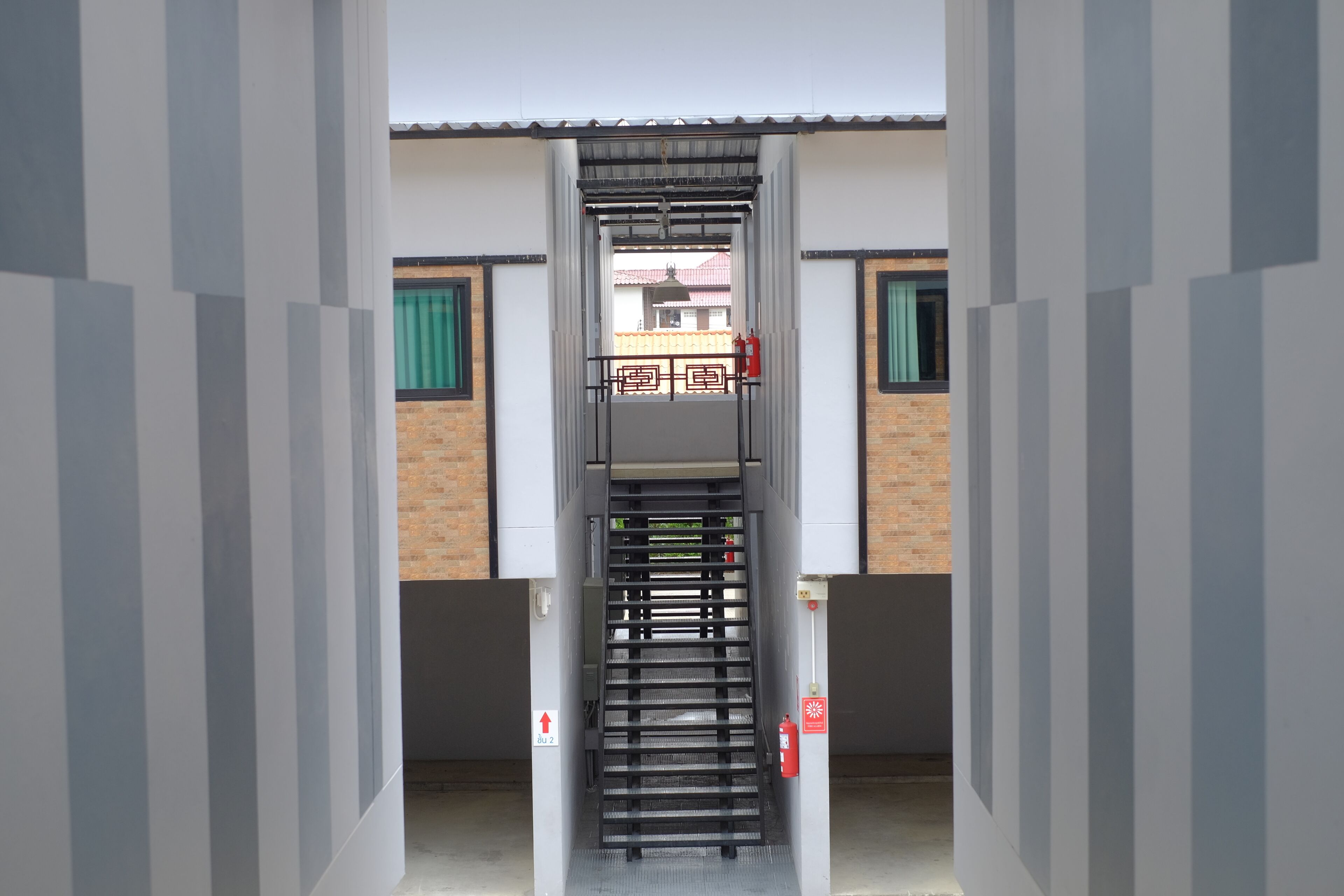 Eine Treppe führt zu einer oberen Etage, gesäumt von Wänden mit einem Feuerlöscher und einer Tür mit einem roten Pfeilschild.
