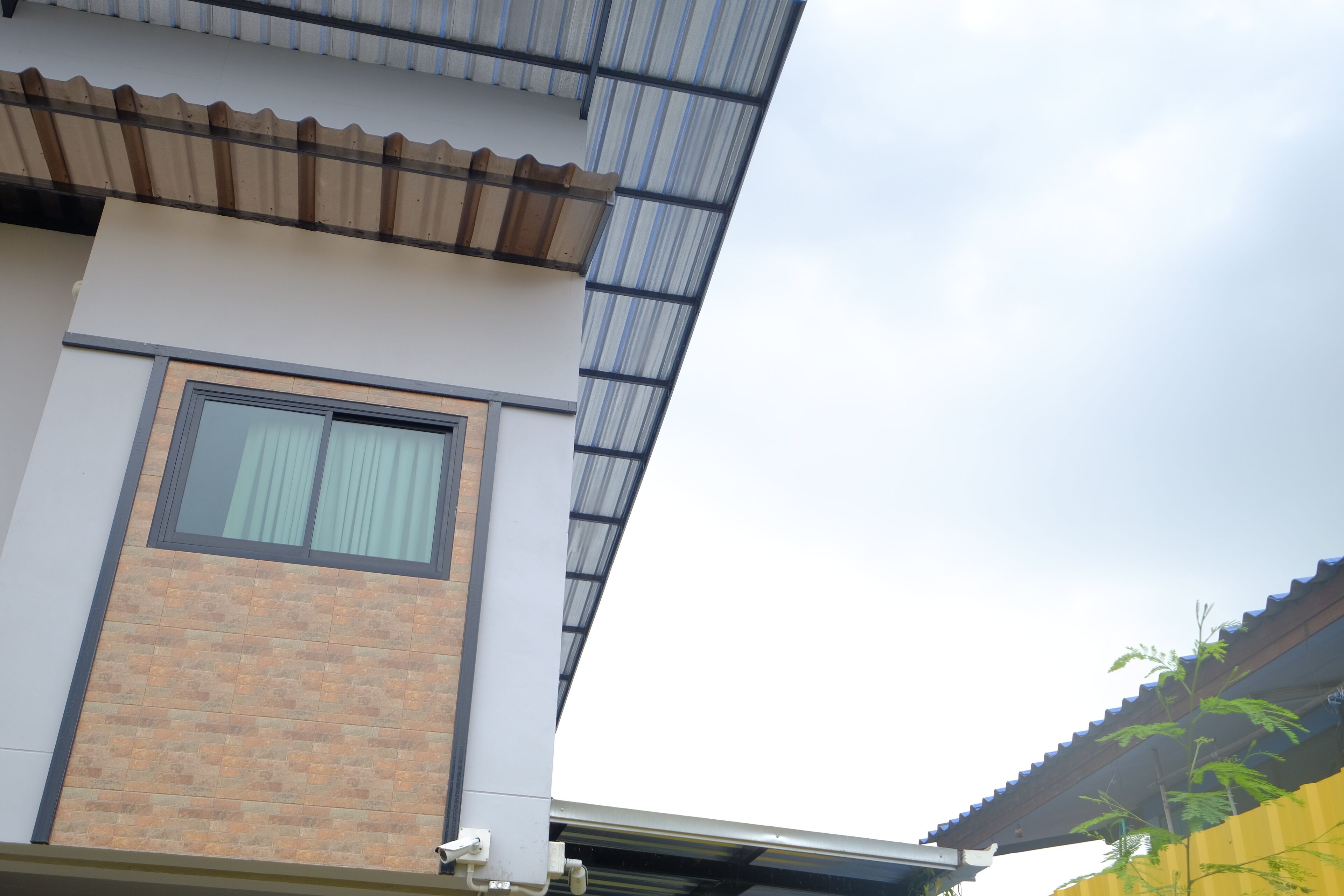 A building with a brick facade, a large window with curtains, and a corrugated metal roof.