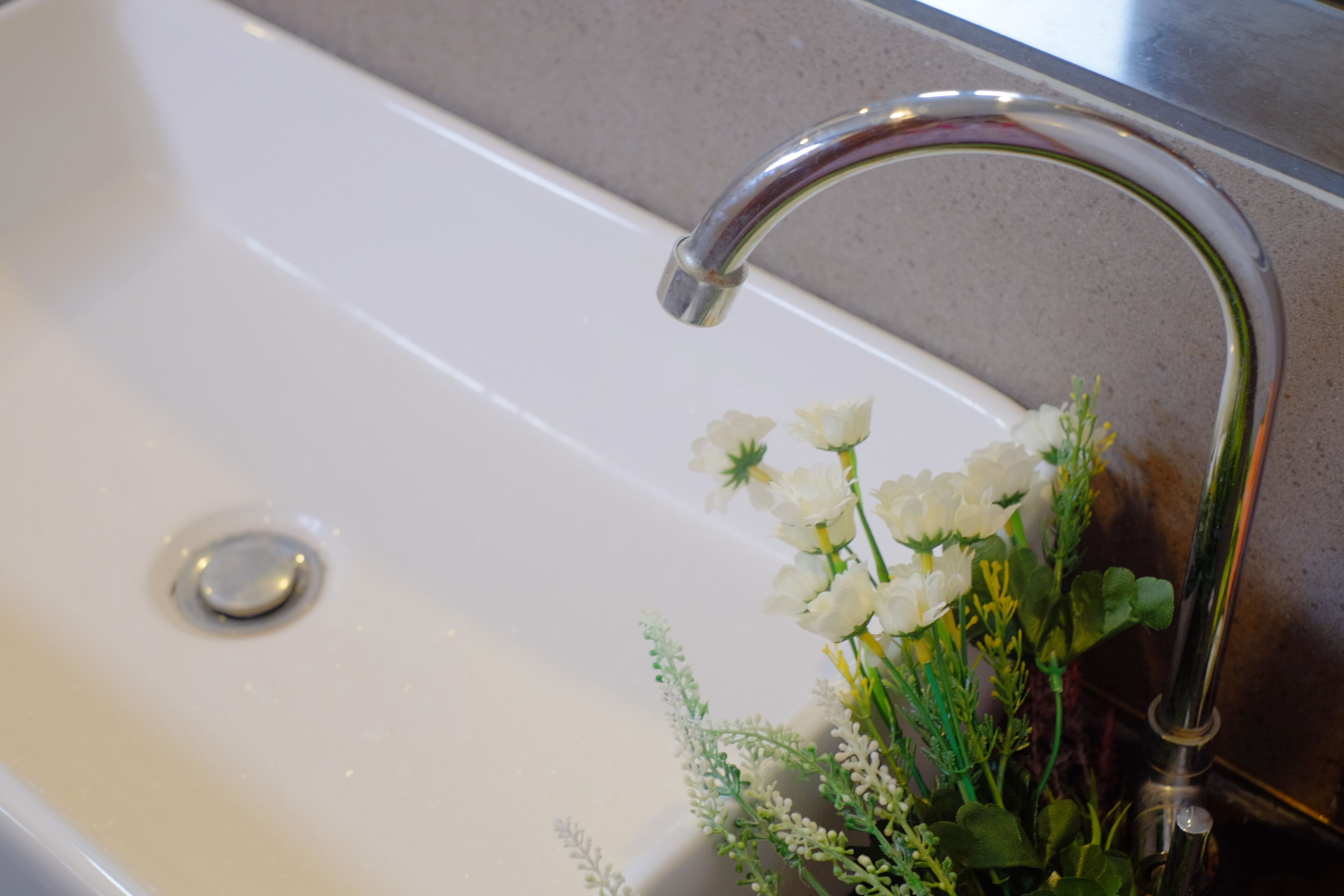 A bathroom sink with a chrome faucet and a flower arrangement beside it.