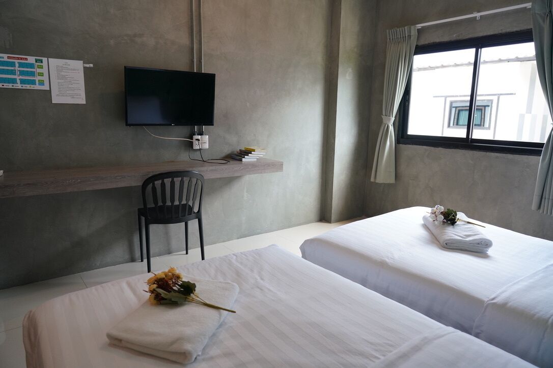 Una habitación de hotel con dos camas, un escritorio con silla, televisor y ventana con cortinas.