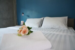 A neatly made bed with white linens and a single rose in a vase on the bed.