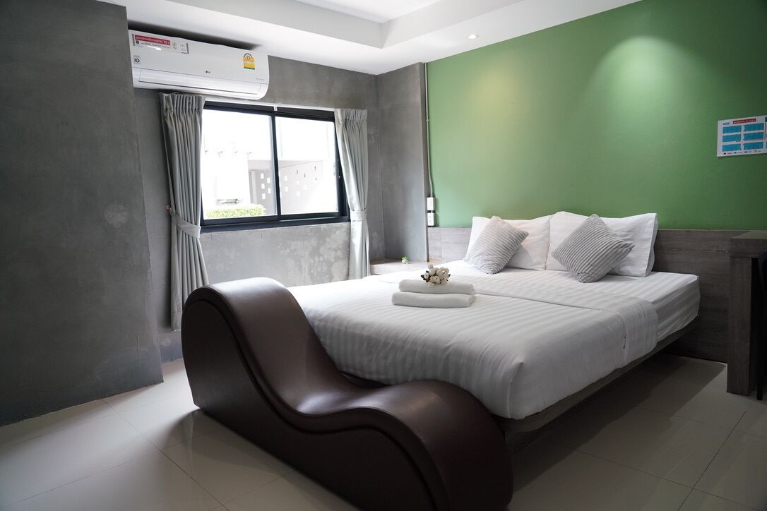 Un dormitorio moderno con una cama grande, paredes grises y una pared de acento verde, además de una ventana con cortinas.
