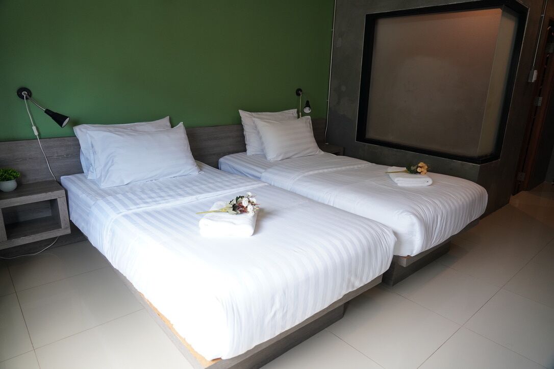 A hotel room with two beds, a green wall, and a large window.