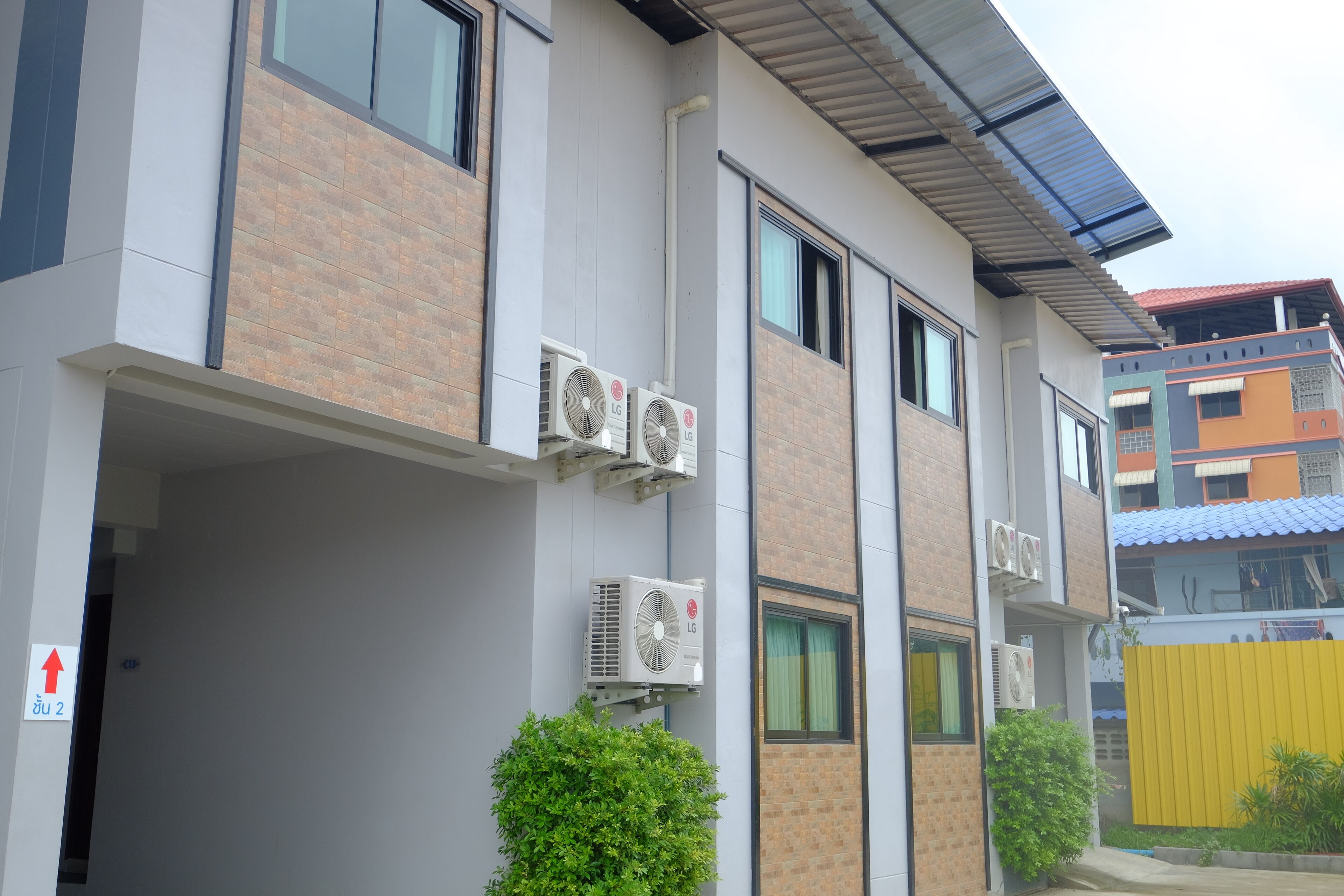 Un edificio moderno con varios equipos de aire acondicionado, una cerca amarilla y un pequeño arbusto verde.