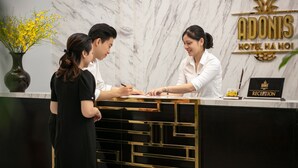 Ein Empfangstresen im Adonis Hotel, mit Marmorwand im Hintergrund und einem Schild, das den Empfangsbereich kennzeichnet.