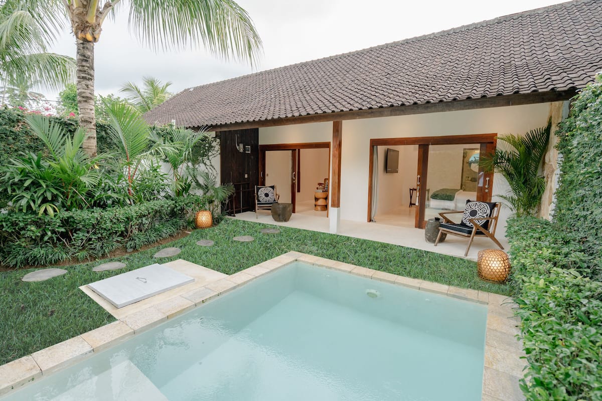 A pool area with a tiled roof, a small pool, and a seating area with a sofa and chairs.