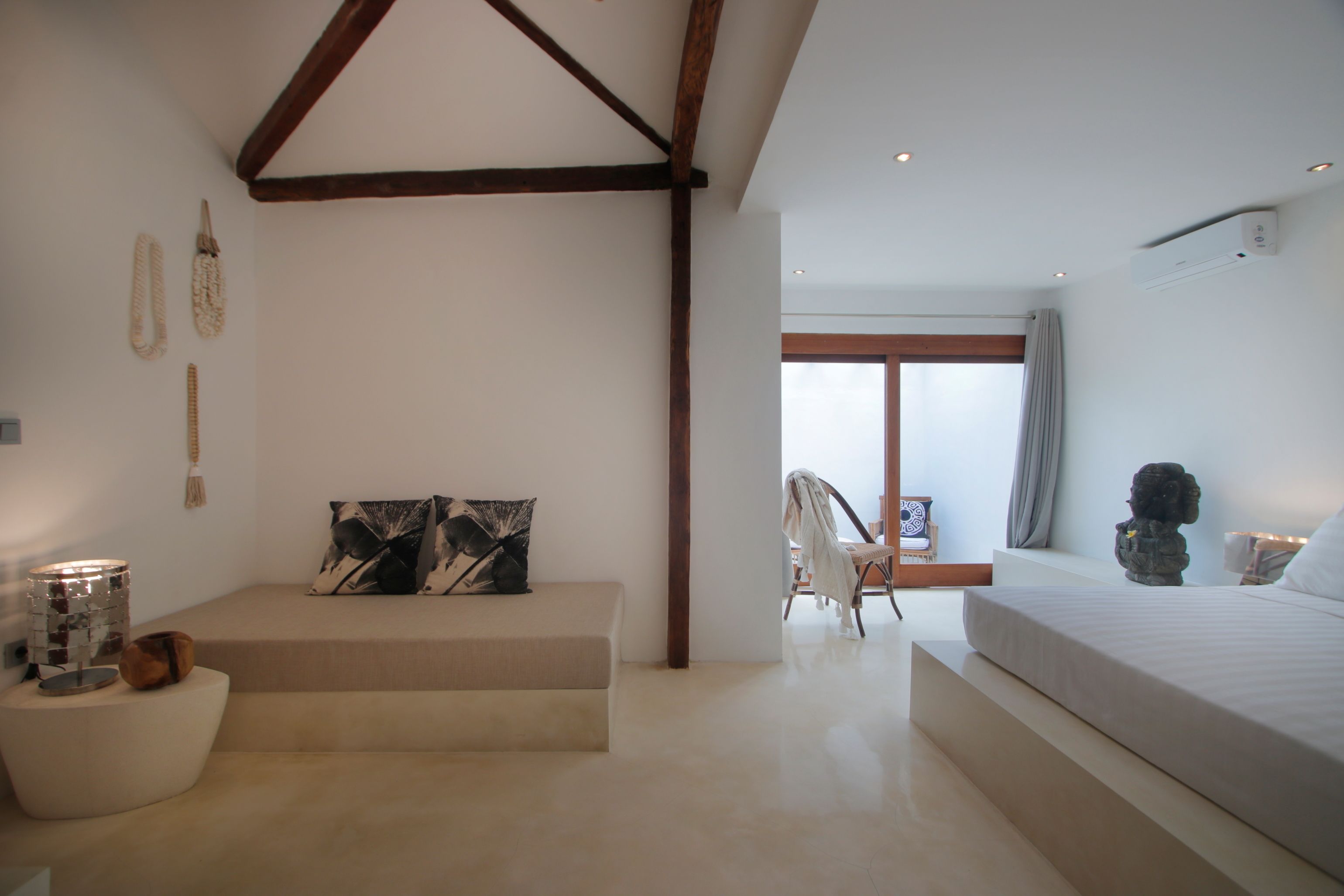 A modern bedroom with a large bed, a seating area with a bench, and a view of the outdoors through a large window.